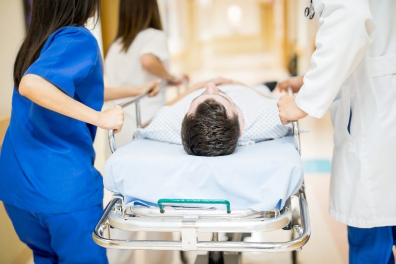 Rear view of a male patient being transported in a stretcher by a group of doctors in a hospital hallway