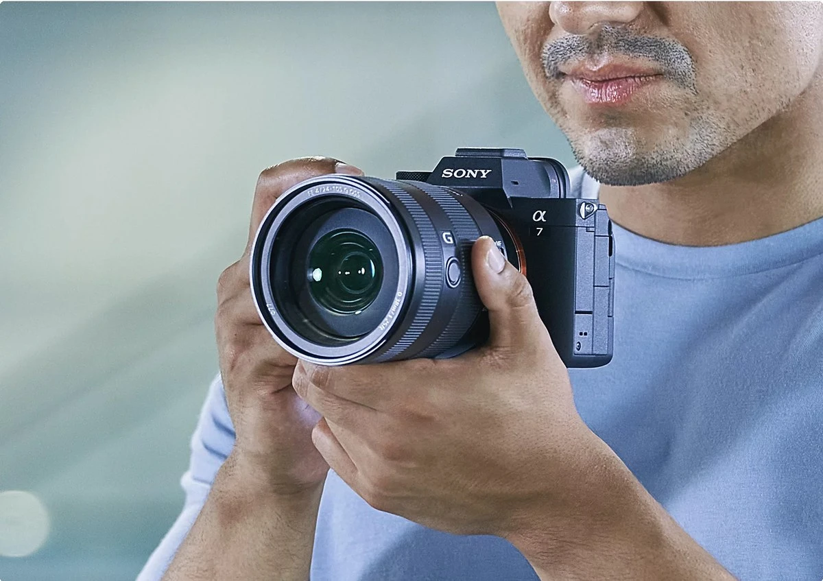 Руки фотографа тримають камеру Sony Alpha 7 IV на рівні обличчя в положенні візування через видошукач